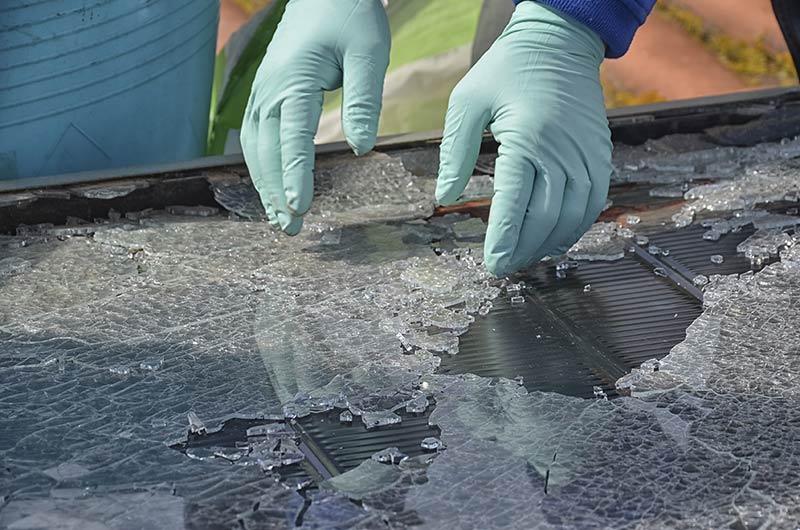 two gloved hands picking up broken glass from a solar panel